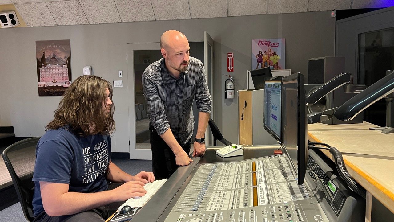 Two men are working on a sound board in a studio.