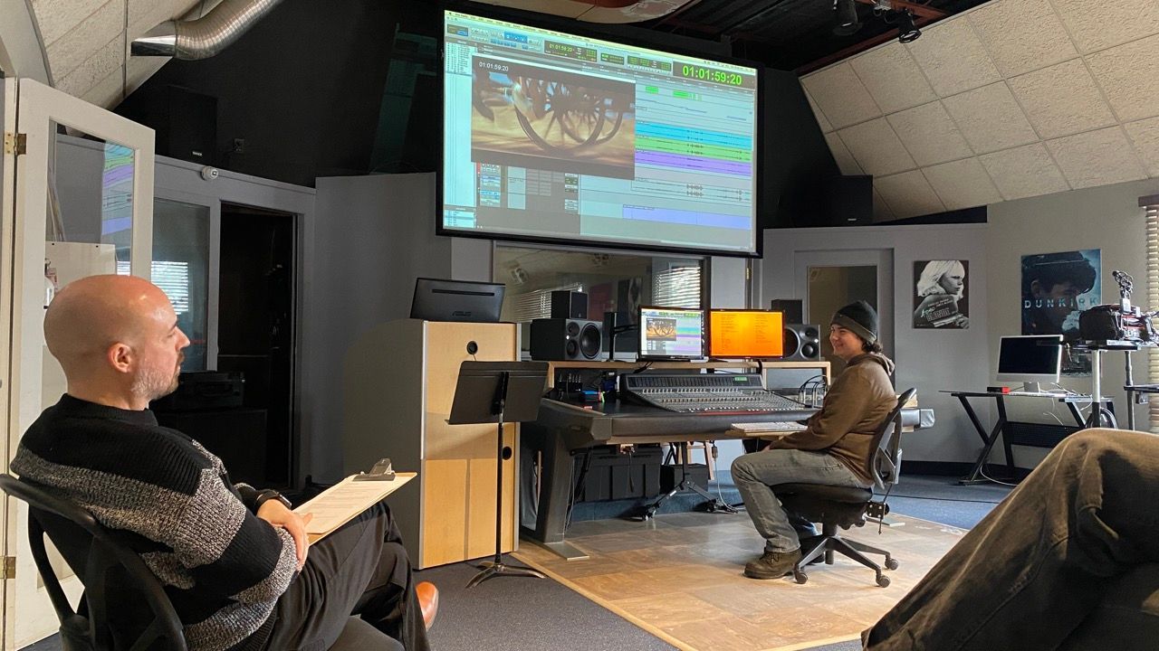 Two men are sitting in a room in front of a projector screen.