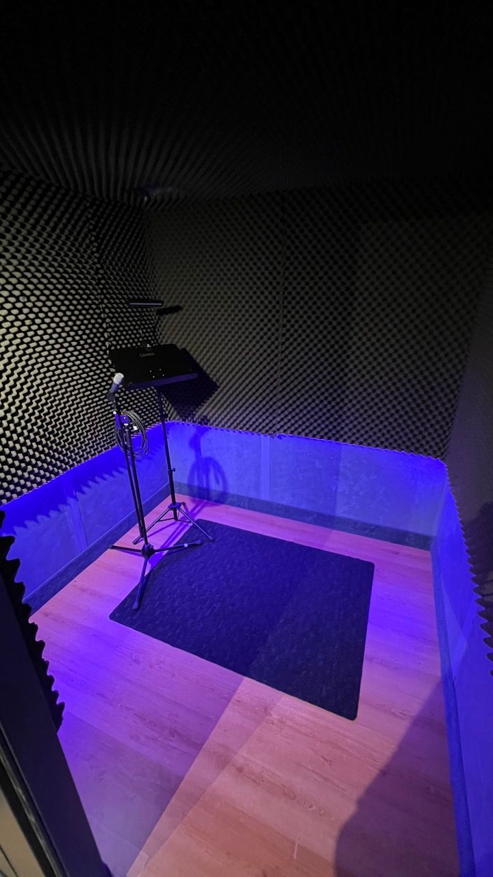 Recording booth with acoustic foam walls, a music stand, and a blue-lit floor.