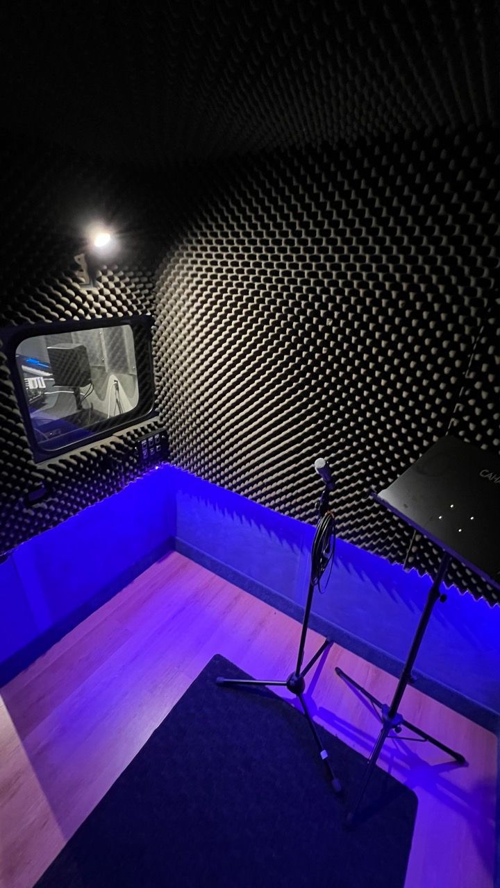 Small recording studio with soundproof foam walls, a microphone, and blue ambient lighting.