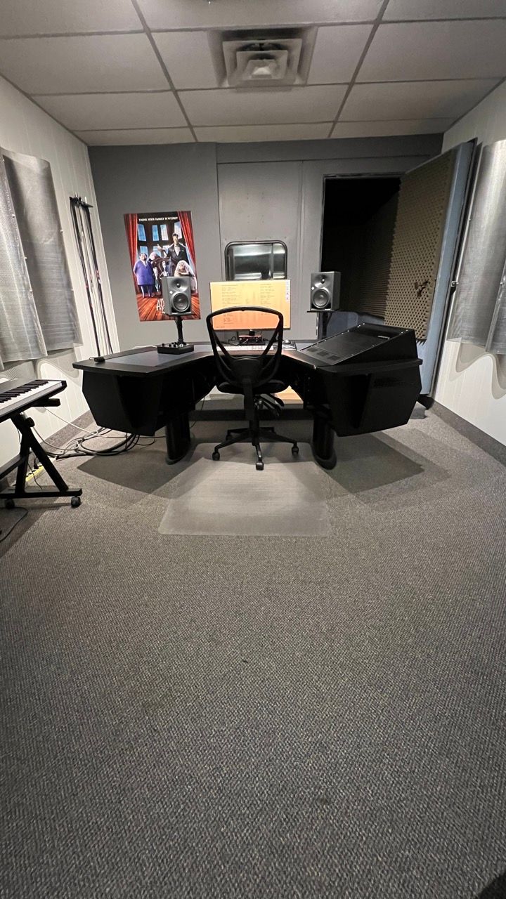 Recording studio with black desk, chair, equipment, and soundproofing on walls.