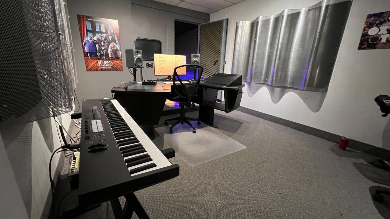 Recording studio with keyboard, computer desk, soundproofing panels.
