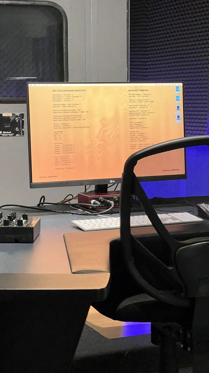 Computer monitor displaying code on a desk with a keyboard, chair, and audio equipment in a dimly lit room.