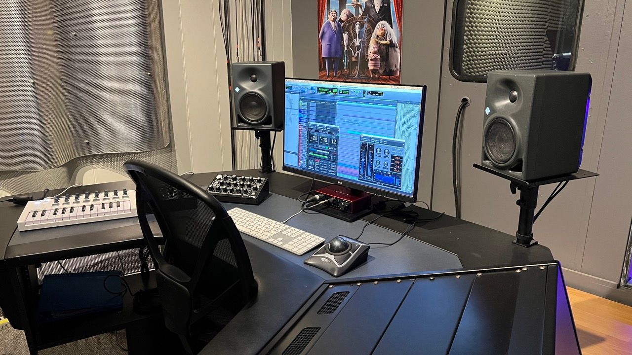 Music studio desk with monitor, speakers, keyboard, and audio equipment.