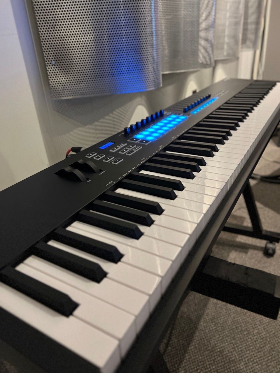 Black keyboard controller with glowing blue lights on a black stand.