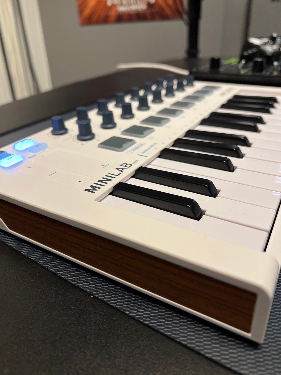 White MIDI keyboard with wood trim and blue knobs on a desk.