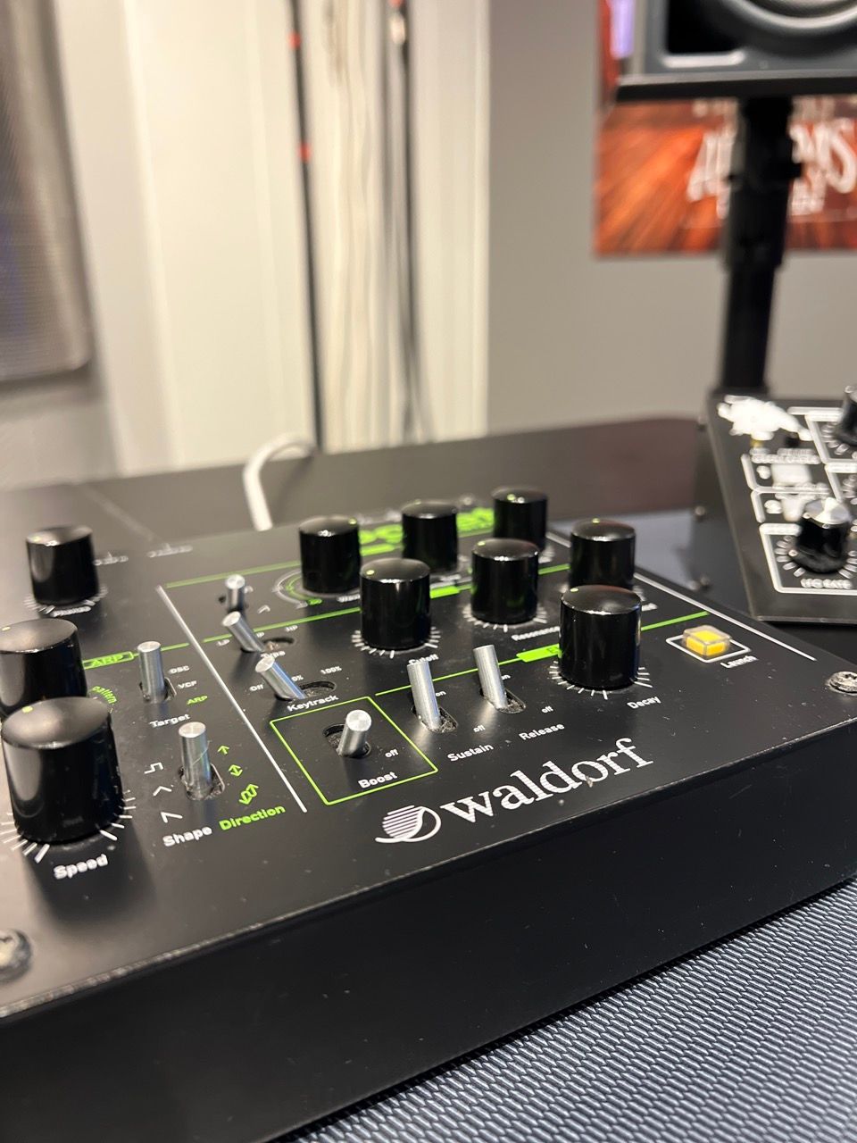 A black Waldorf audio mixer with green accents and black knobs, on a table.