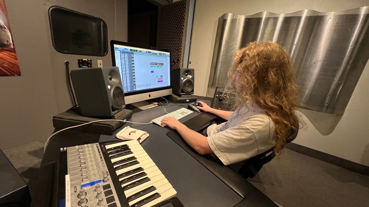 Person using a computer in a sound studio with keyboard and sound equipment.