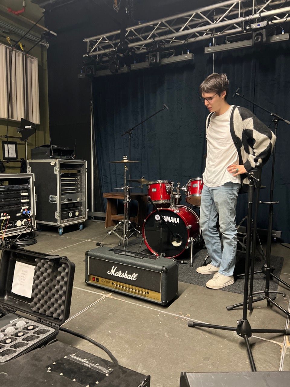 A man is standing in front of a drum set in a room.
