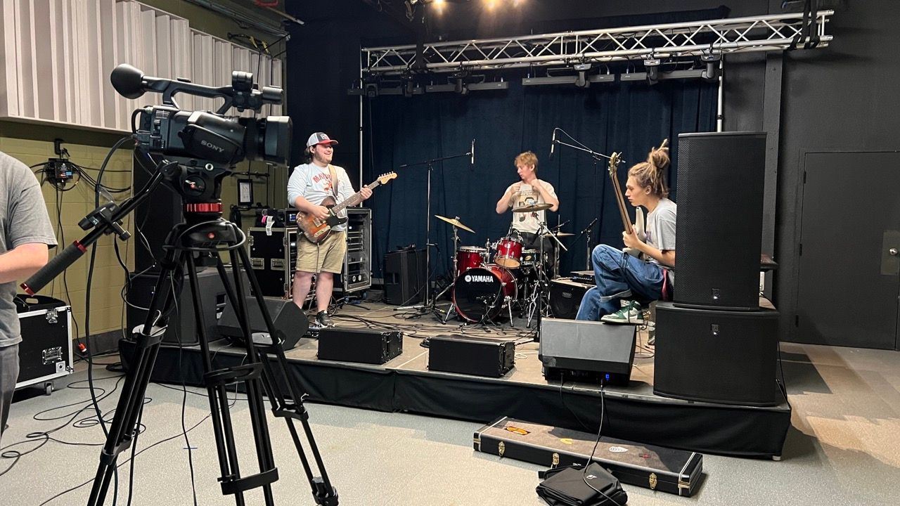A group of people are playing instruments on a stage in front of a camera.