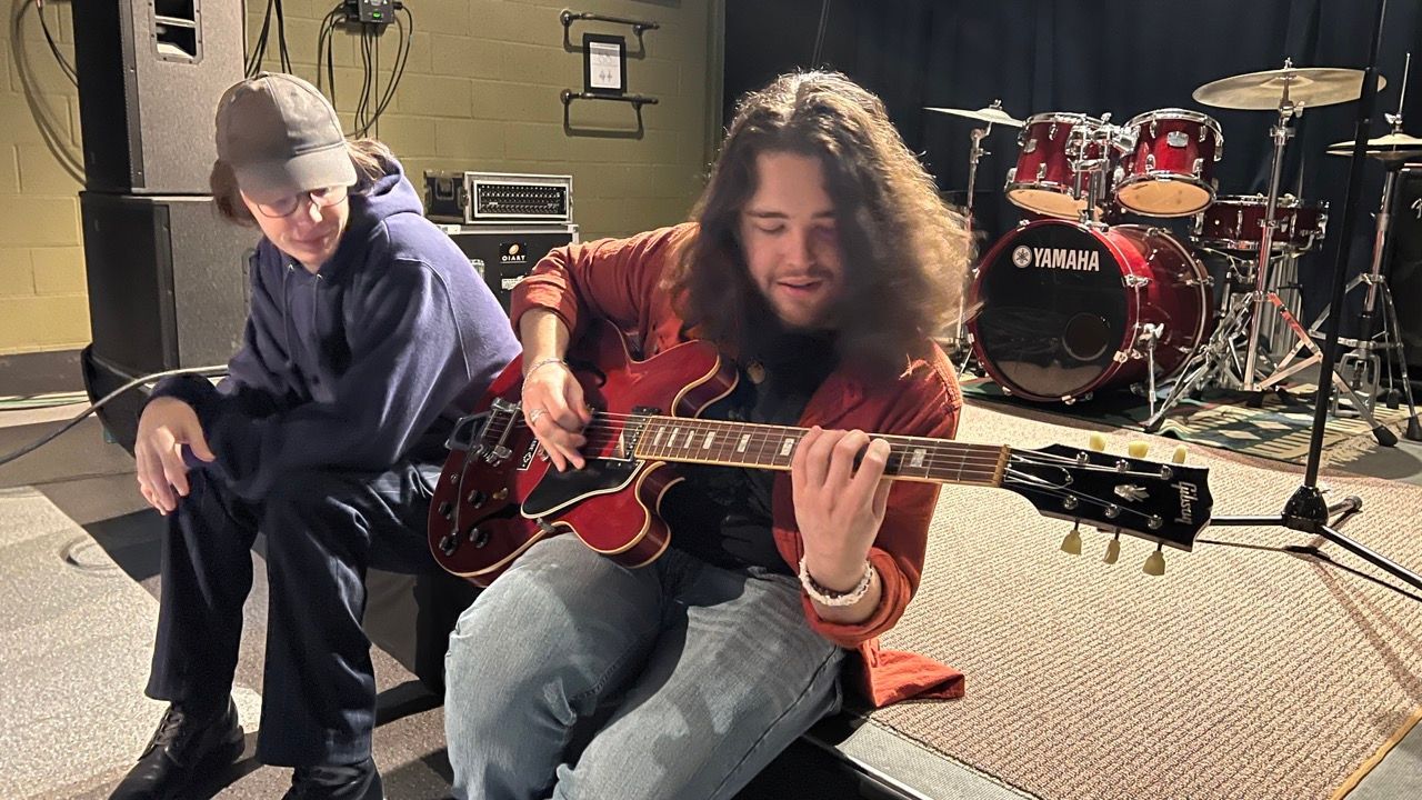 Two men are playing guitars in front of a drum set.