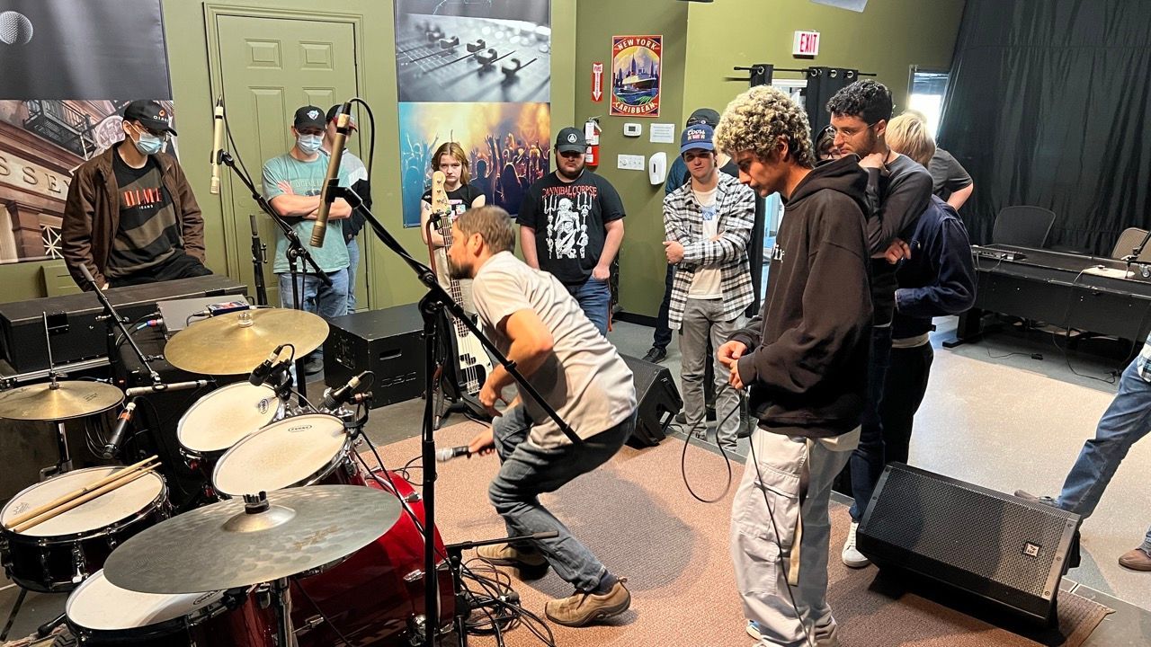 A group of people are standing around a drum set in a room.