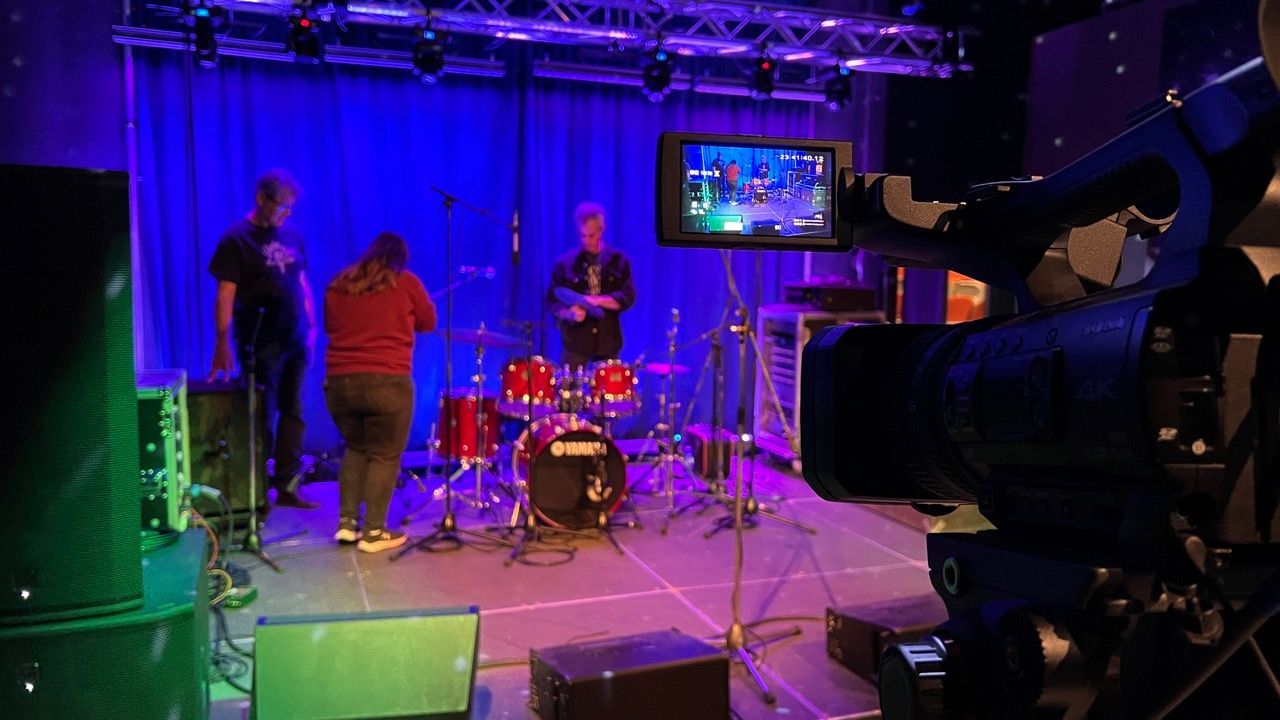 A group of people are playing drums on a stage in front of a camera.