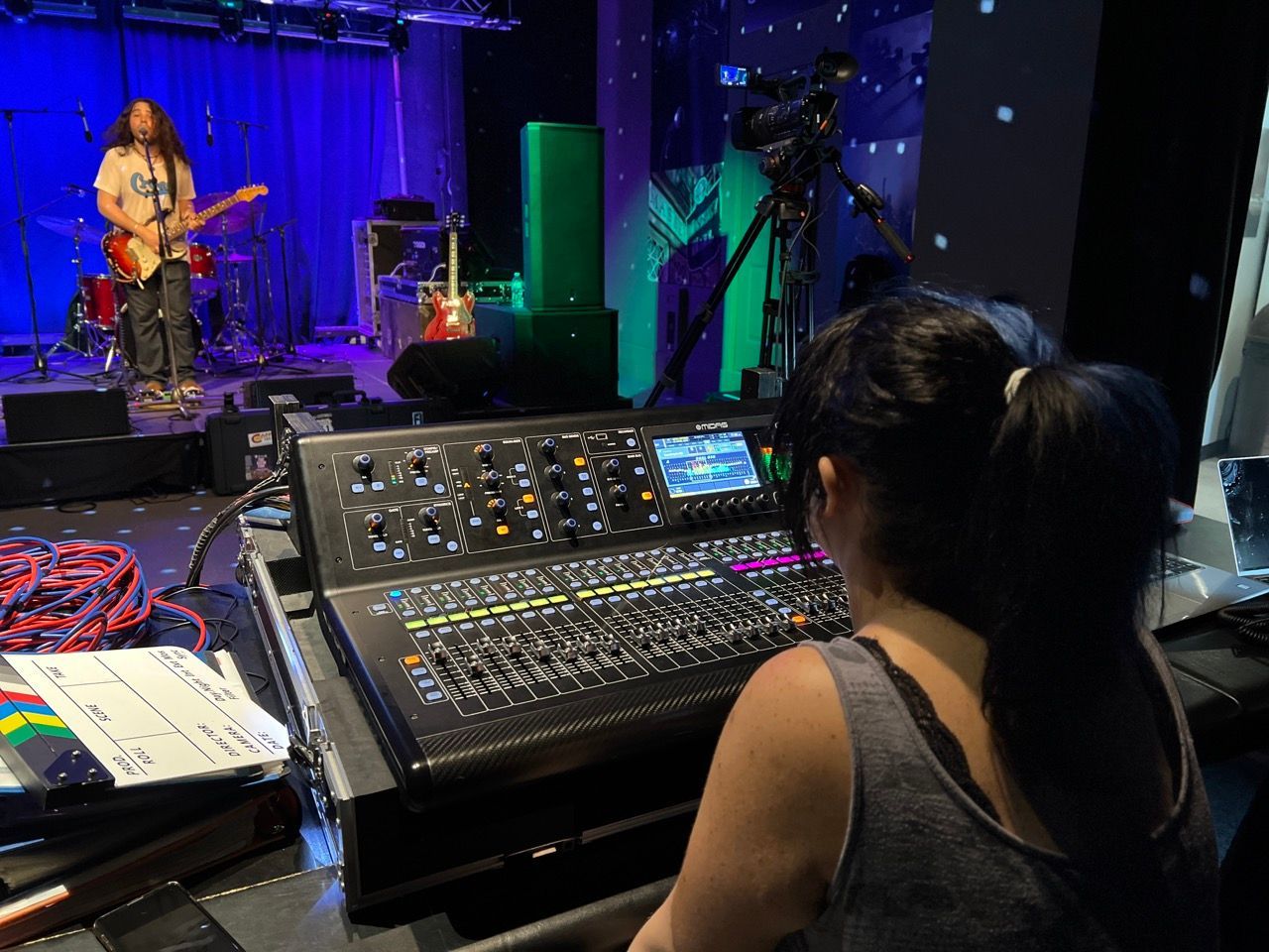 A woman is sitting at a mixer in front of a band on stage.