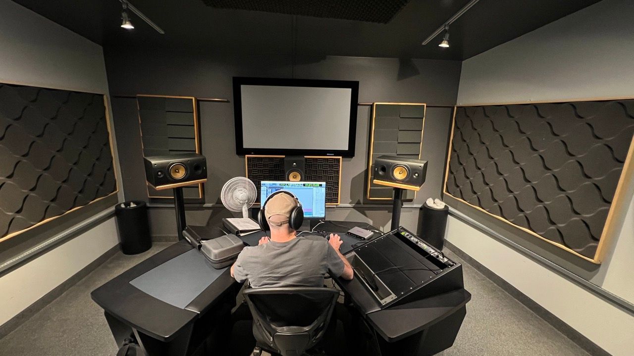 Person at a computer in a soundproof room, surrounded by speakers and acoustic panels.
