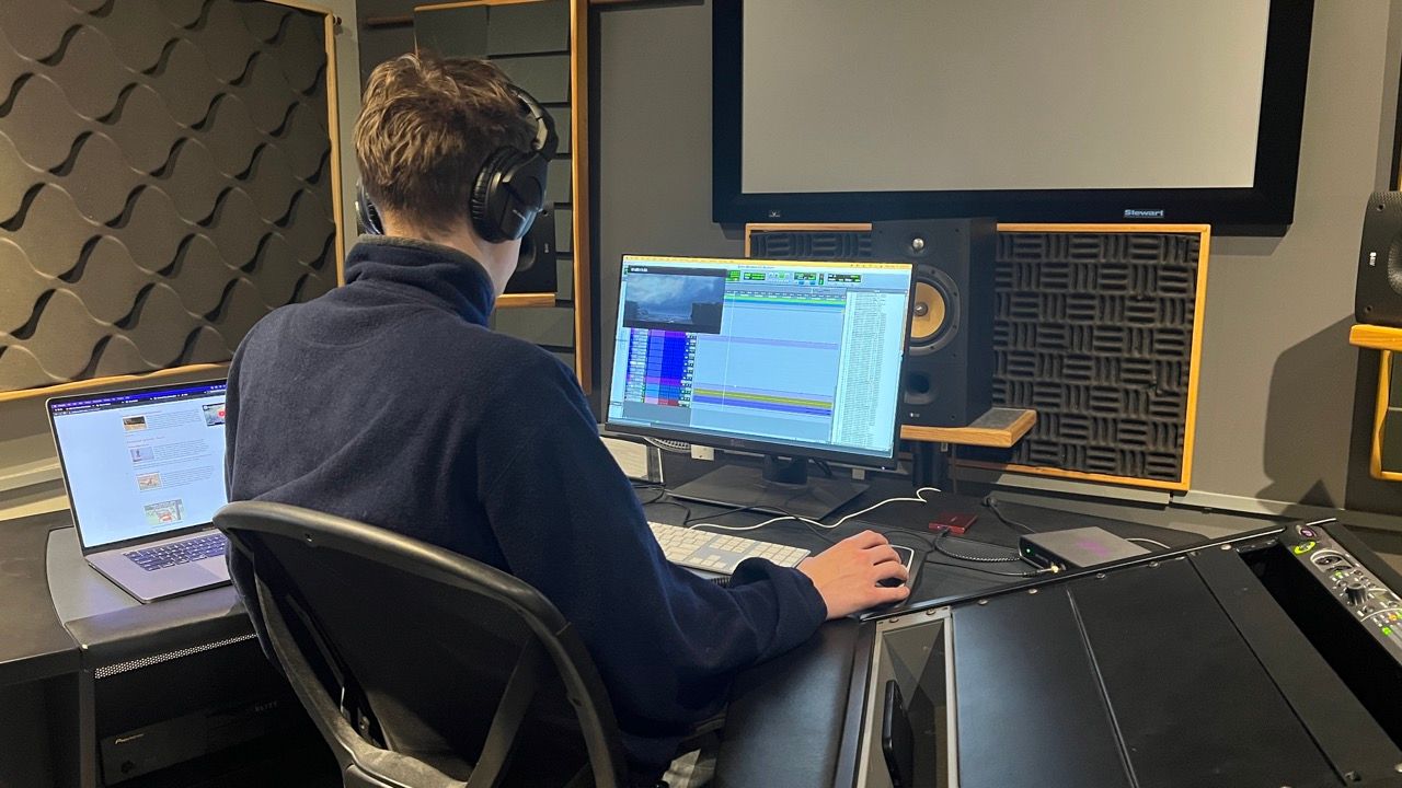 A man is sitting in front of a computer in a recording studio.