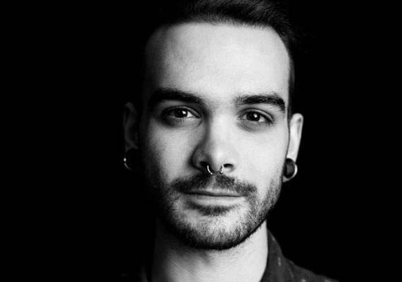 Alex Robillard with dark hair, nose ring, and ear gauges, looking directly at the camera.