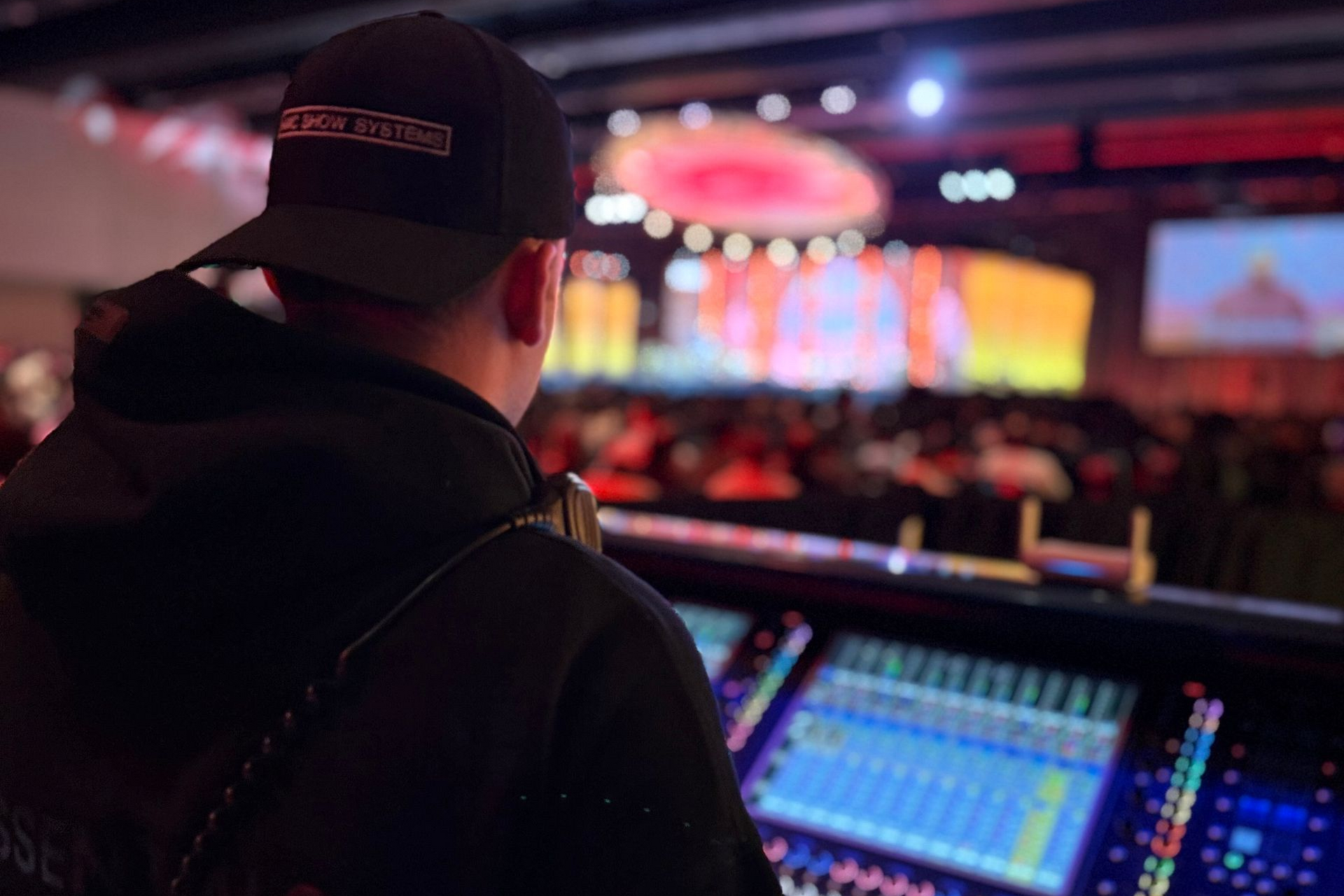 Avery Szumlanski an audio technician at a mixing console facing a brightly lit concert stage during a live event