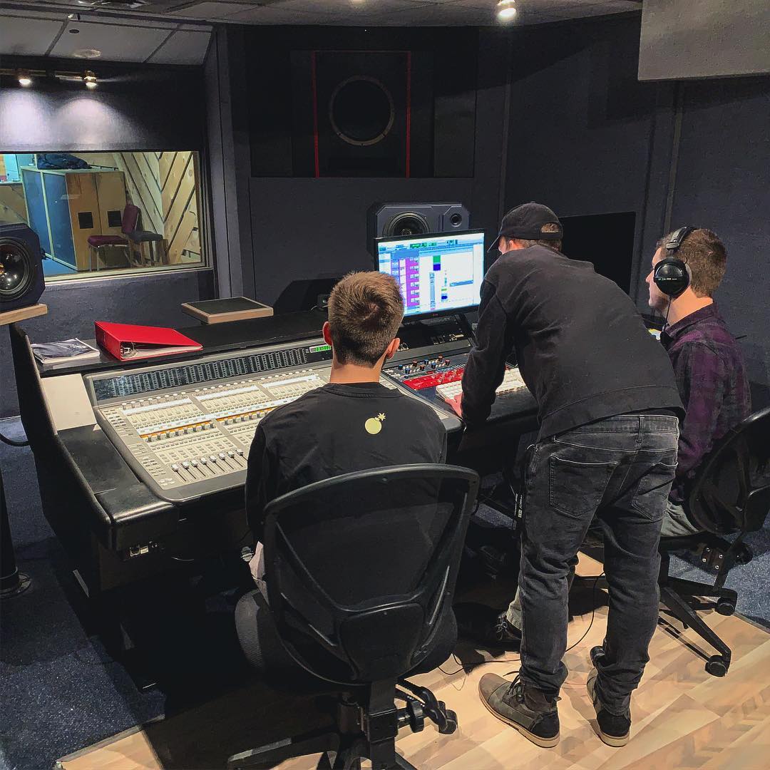 A group of men are working on a computer in a recording studio.
