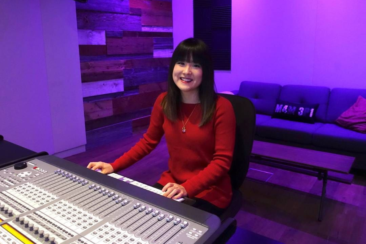 Michelle in red sweater seated at a mixing console in a purple-lit recording studio