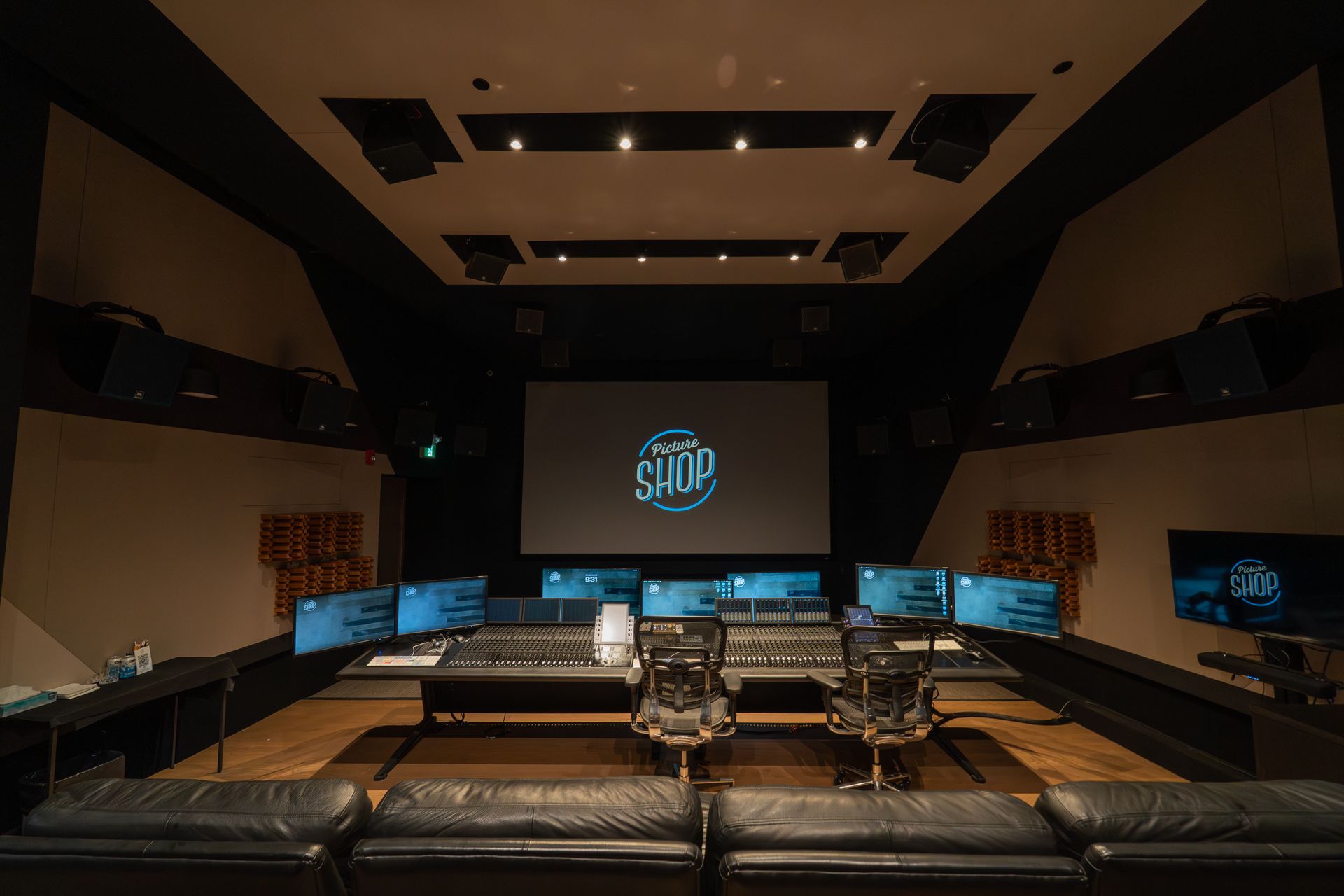 Avery & another working at a large audio mixing console in a studio, with monitors and equipment around them