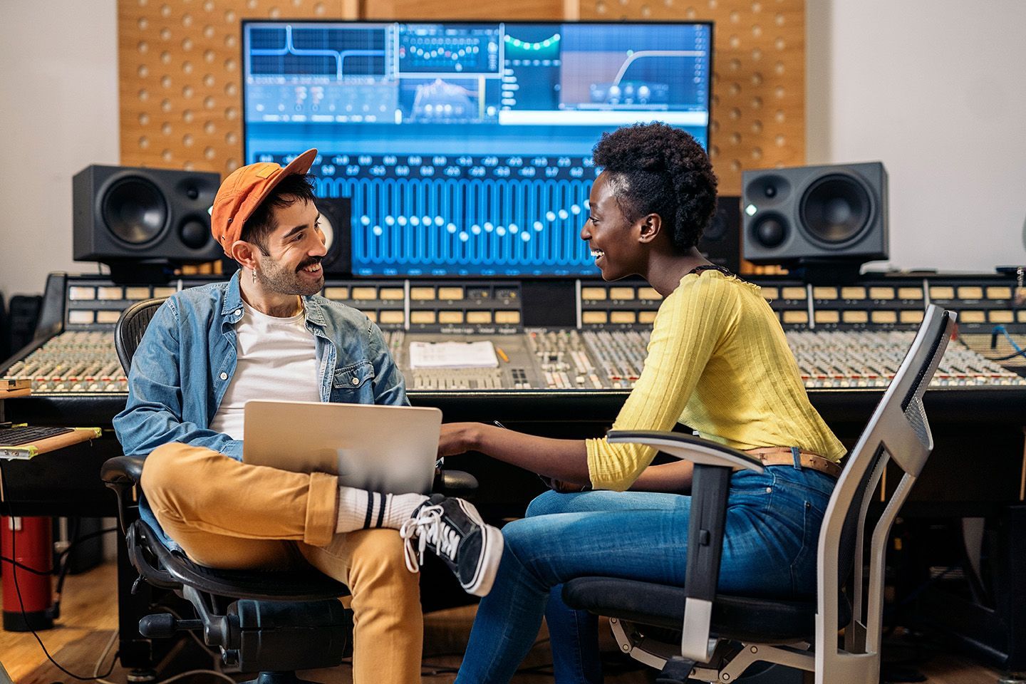 a man and a women discussing music production in front of a sound board in a studio