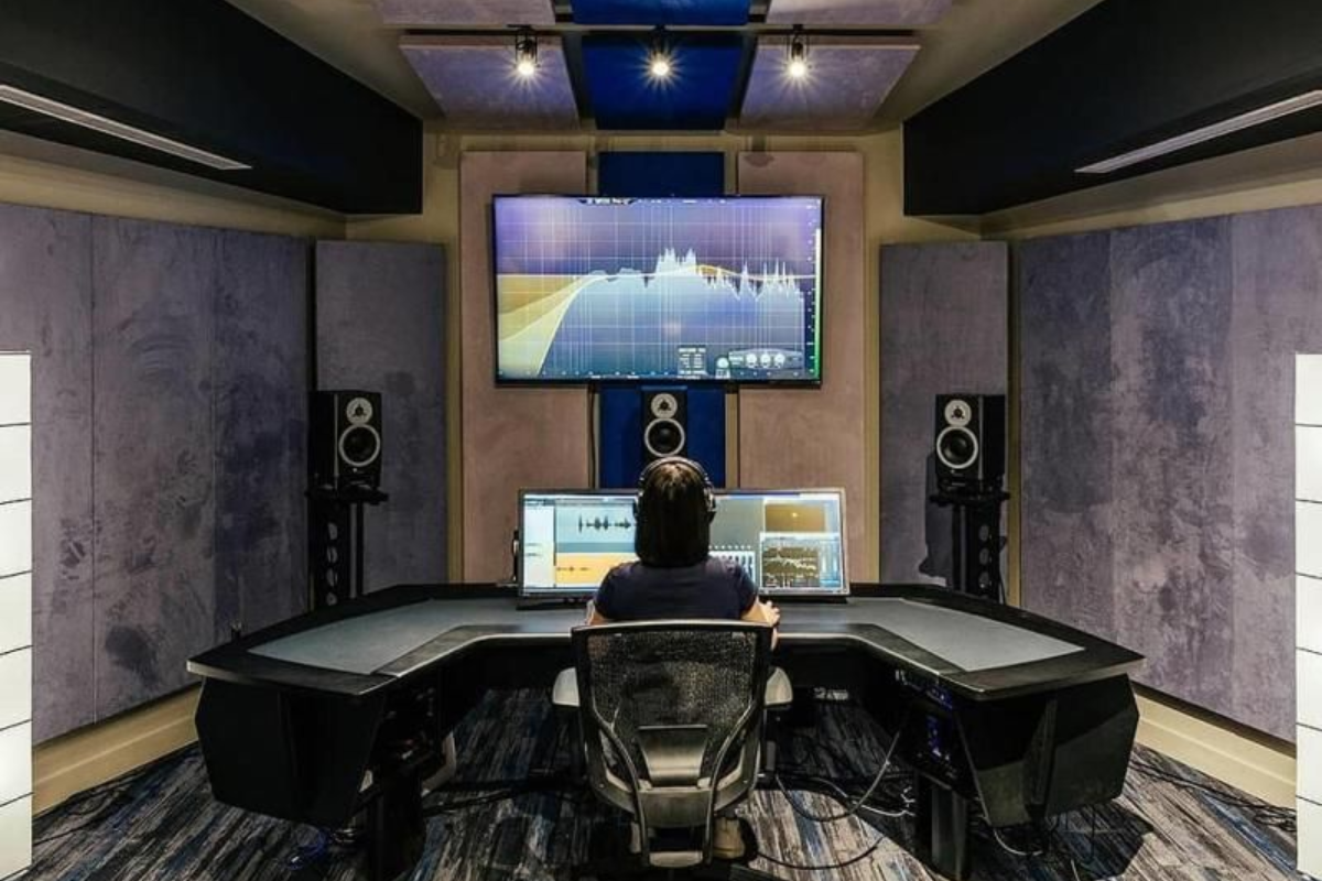 Michelle seated at a studio mixing desk facing large monitors in a modern recording room