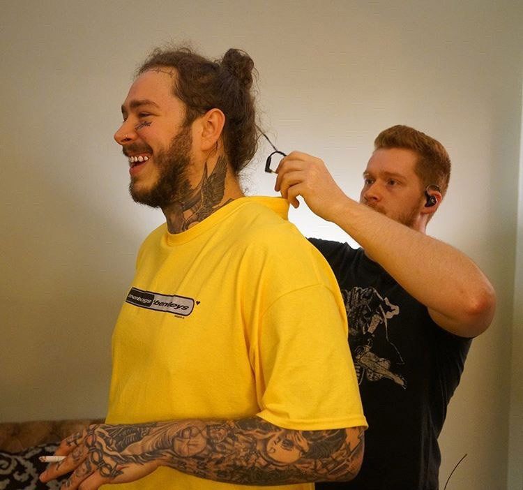 A man in a yellow shirt is getting his hair cut by another man