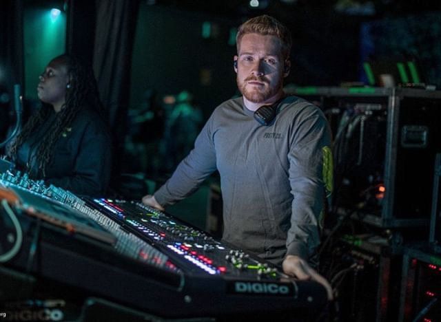 A man is standing in front of a mixer in a dark room.