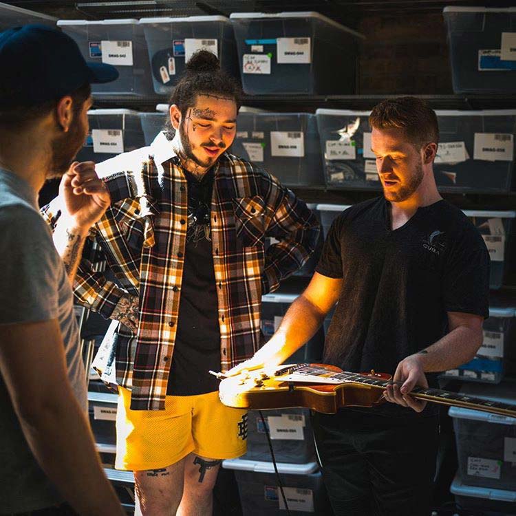 A man in a plaid shirt is playing a guitar in front of a group of men