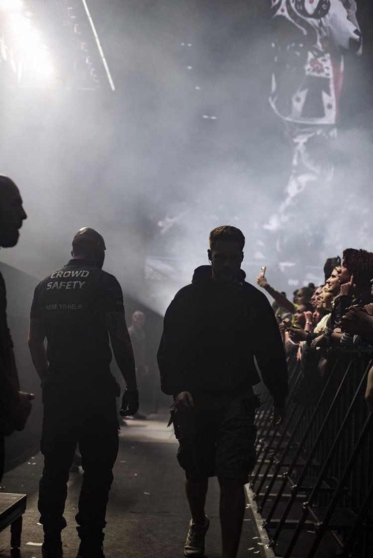 Two men are walking in front of a crowd of people at a concert.