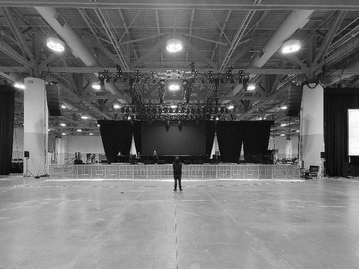 Empty indoor arena with stage lighting and a Avery Szumlanski standing in the center.