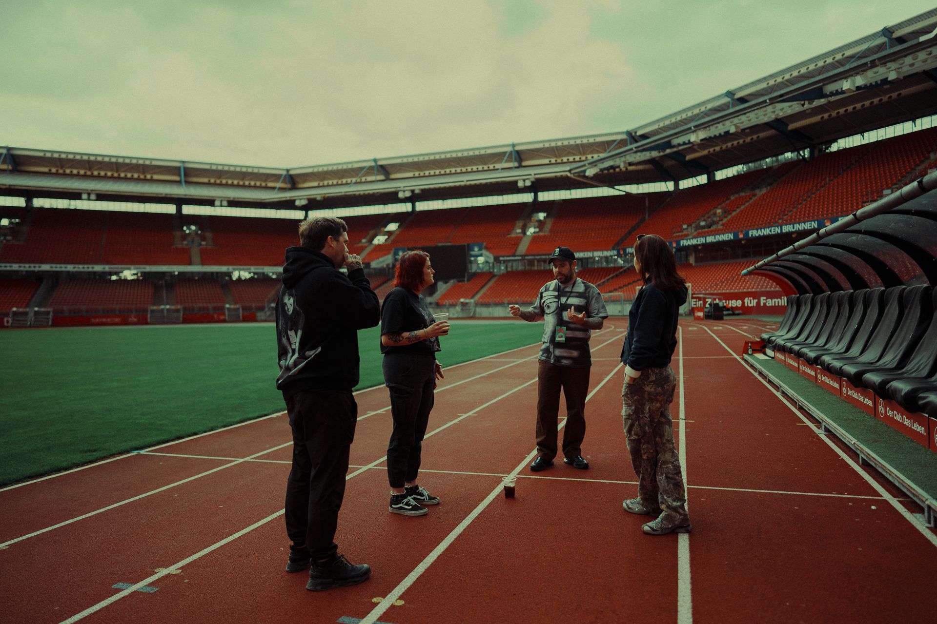 Four people standing on a running track inside an empty stadium, talking near the lanes