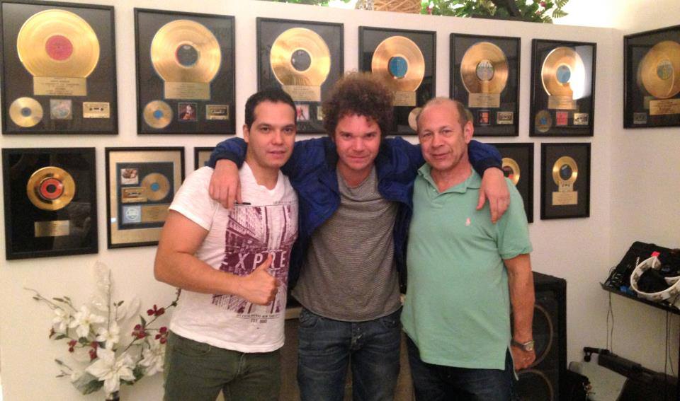 David Lopez and two other people pose with arms around each other, in front of framed gold records.