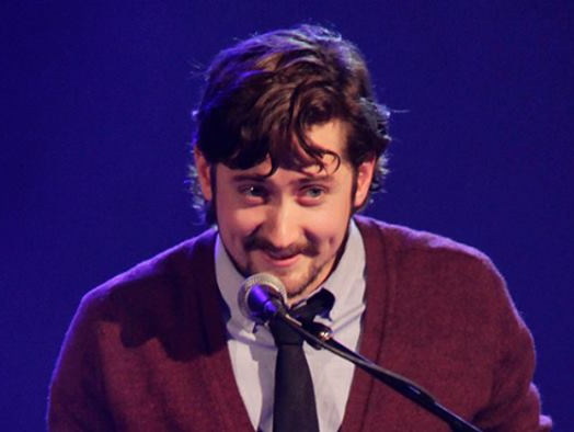 Jesse Ash with a beard is talking into a microphone
