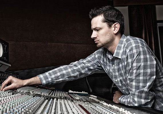 A man in a plaid shirt is working on a mixer in a recording studio.