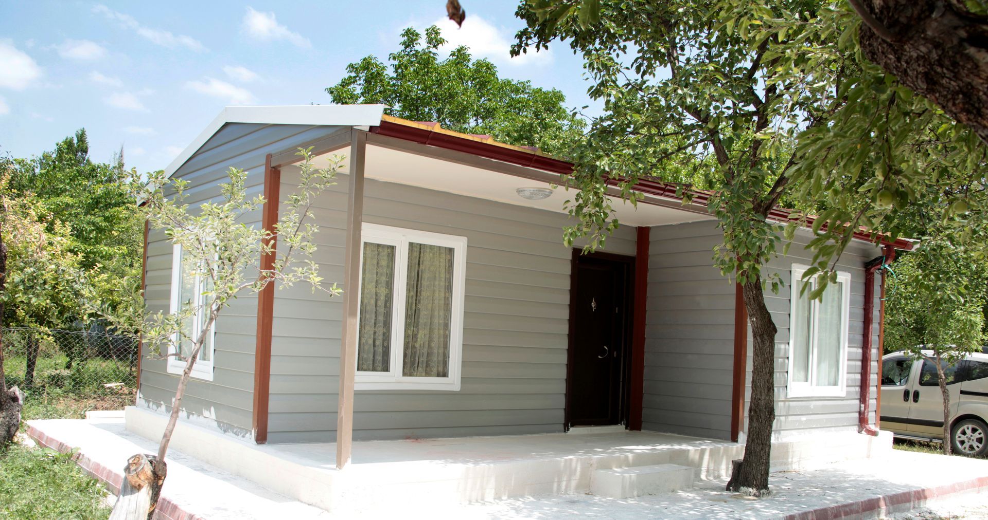 Small gray house with white trim, brown door, and red roof trim.