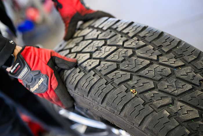 Person wearing red gloves holding a tire with a visible nail.
