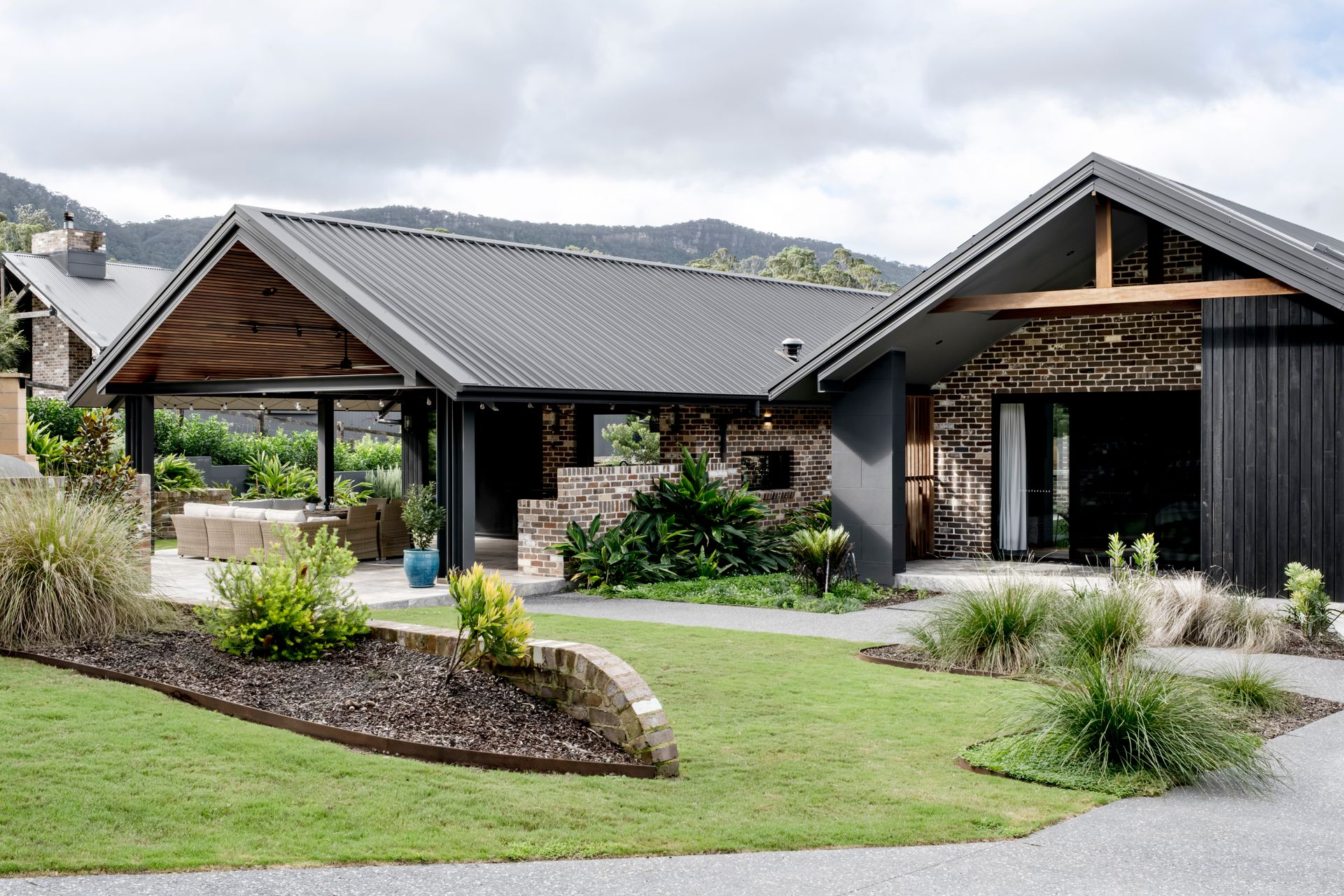 Modern home with dark roof, stone facade, and green landscaping against a mountain backdrop — Evolution Building Group Dapto, NSW