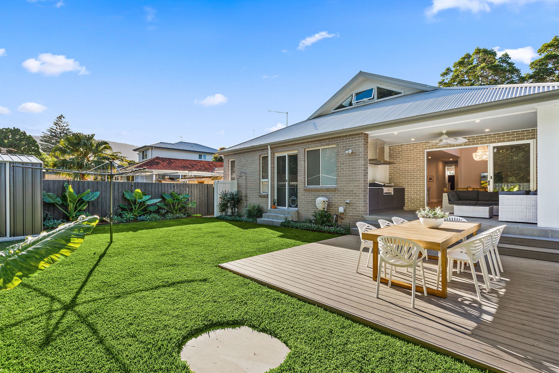 Backyard with a wooden deck and dining table, green lawn, and a modern house with a pitched roof under a blue sky — Evolution Building Group Dapto, NSW