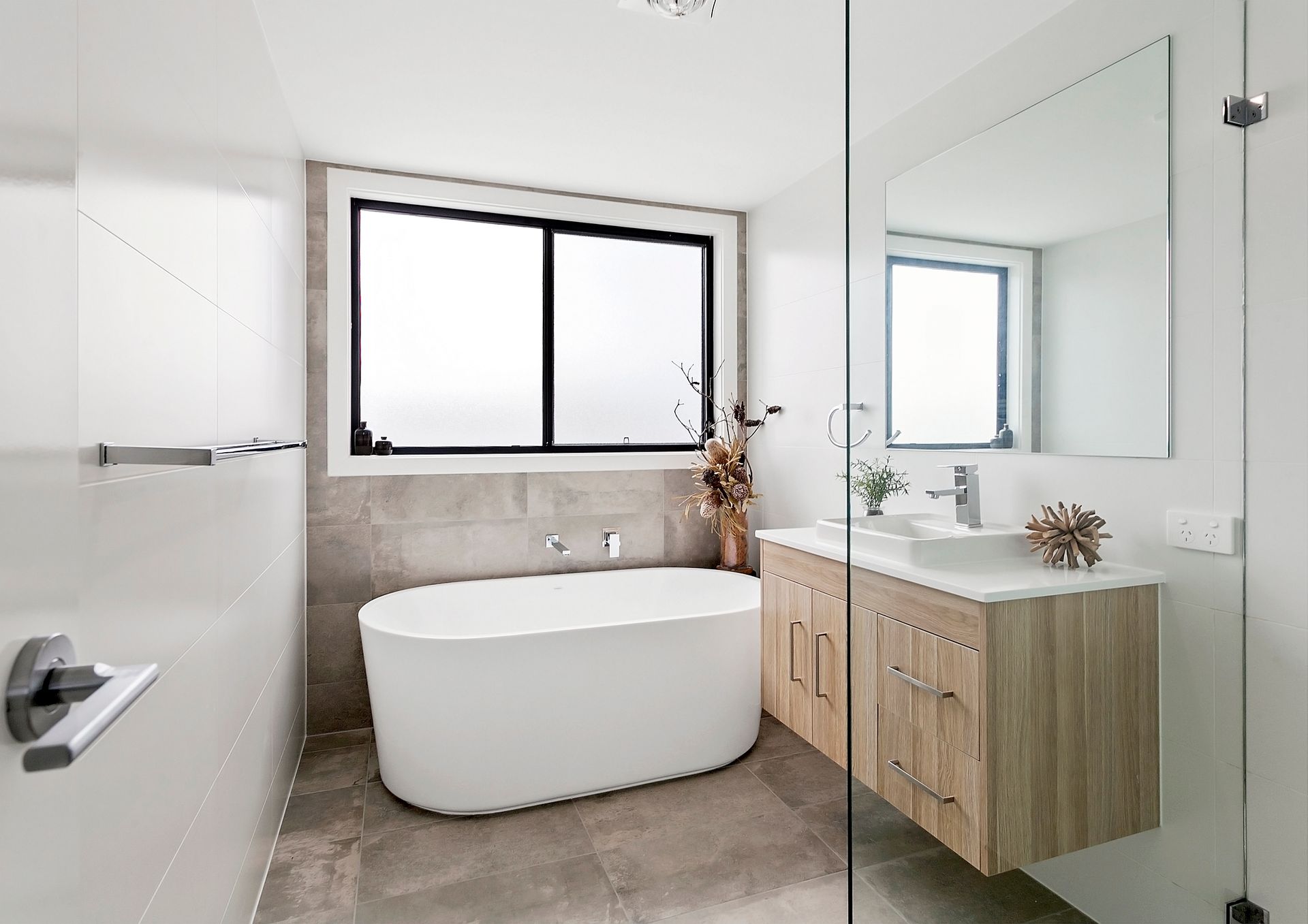 Modern bathroom with a white oval bathtub, a wood vanity, and a large window — Evolution Building Group Dapto, NSW