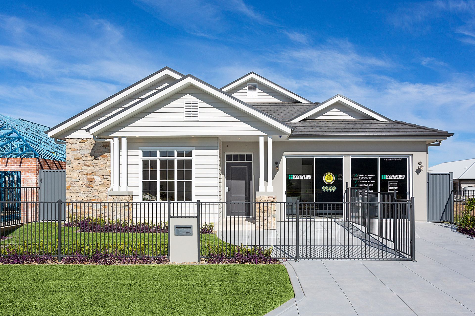 A light-coloured bungalow with a stone accent wall, black fence, and driveway, under a blue sky  — Evolution Building Group Dapto, NSW