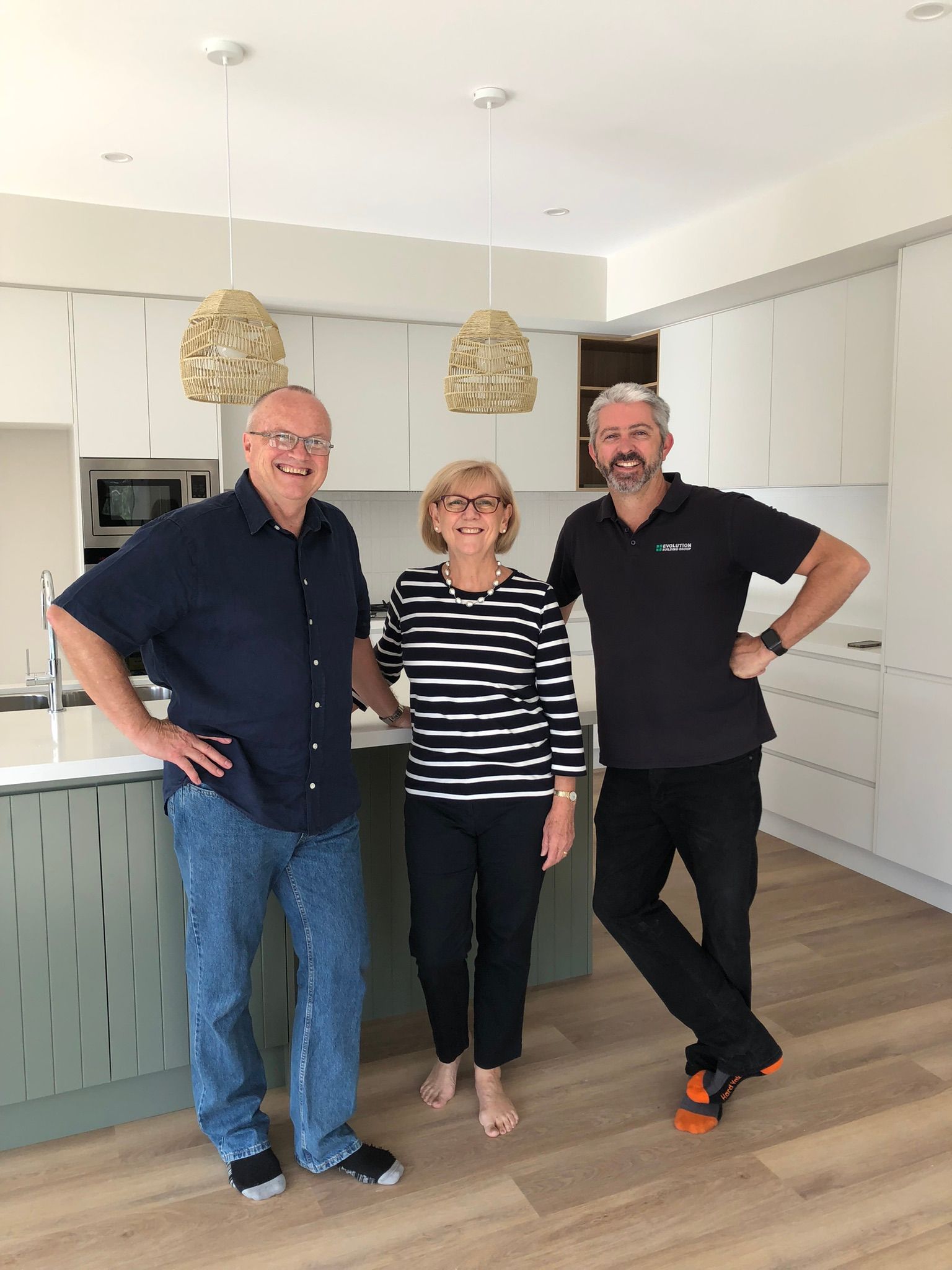 Three people in a modern kitchen with light cabinets. Man with glasses, woman in stripes, and another man — Evolution Building Group Dapto, NSW