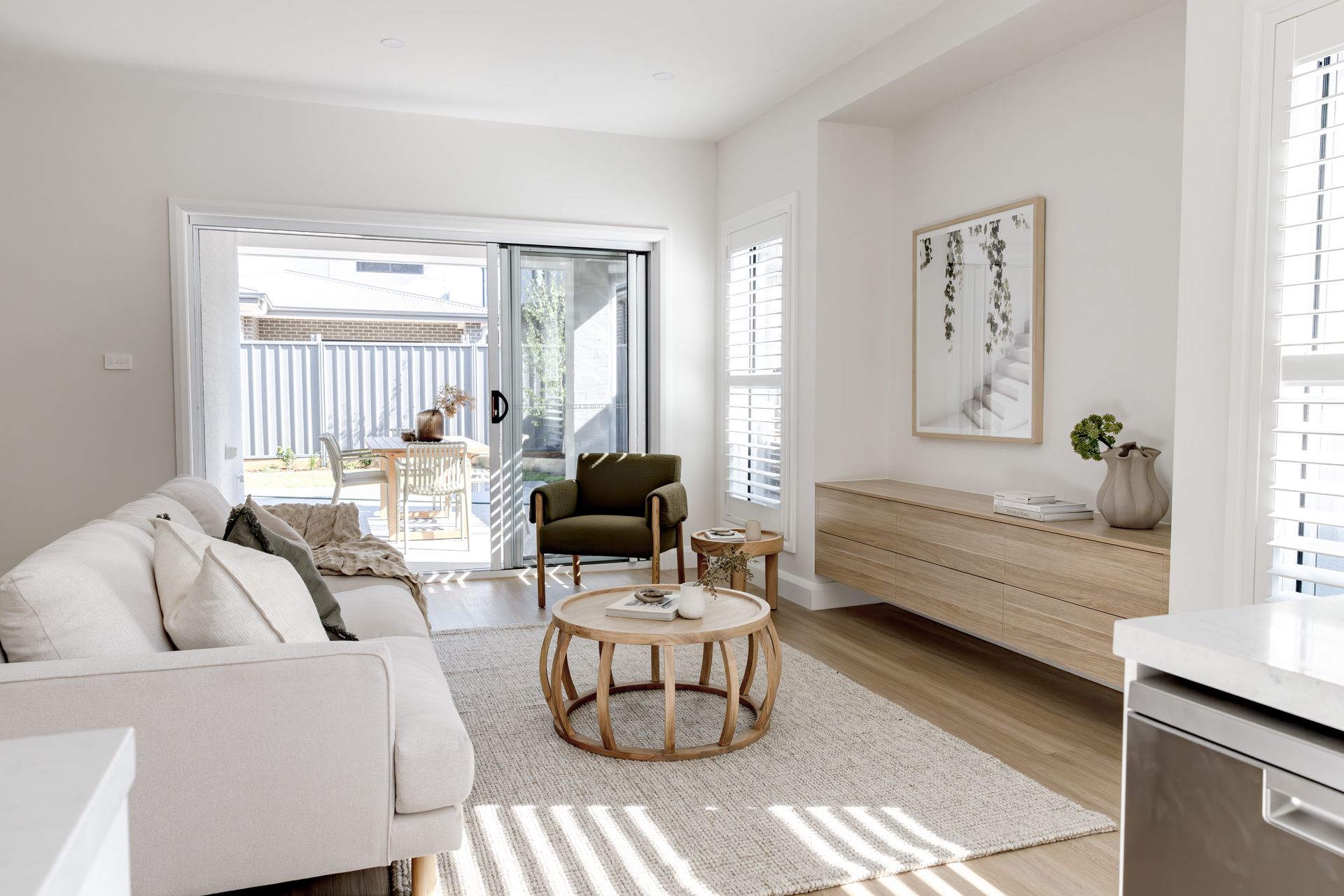 Bright living room with white sofa, olive armchair, wooden coffee table, and sliding glass door to a backyard — Evolution Building Group Dapto, NSW