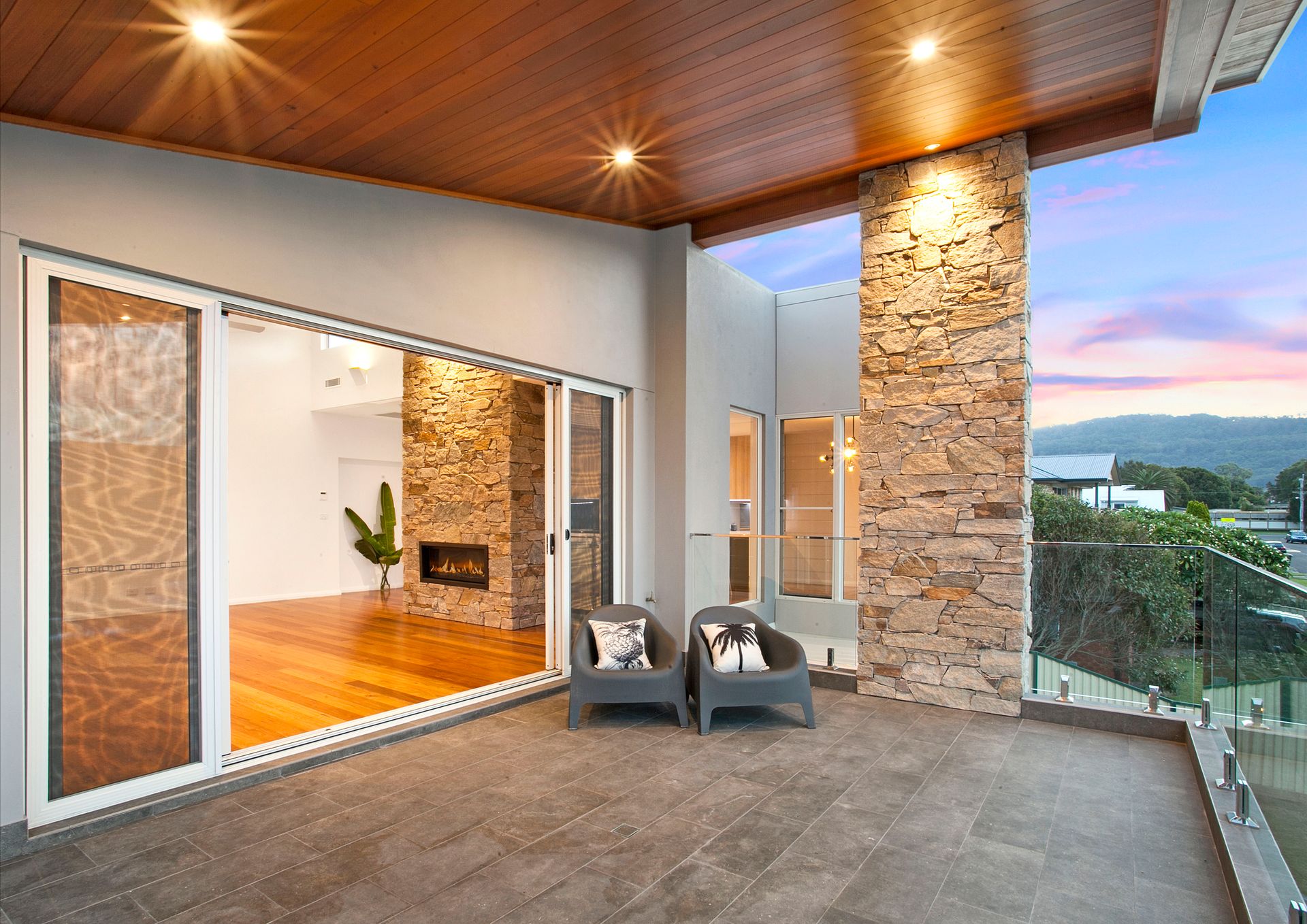 Balcony with open sliding doors leading to a living room. Two chairs sit on the tiled floor, with a stone accent wall — Evolution Building Group Dapto, NSW