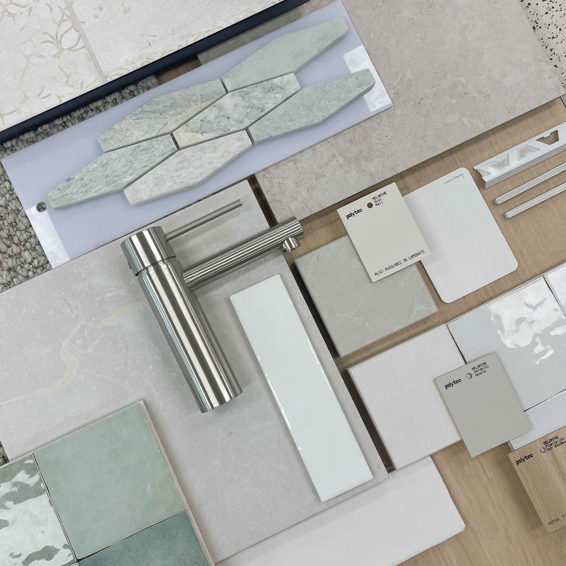 Samples of bathroom tiles and fixtures laid out on a surface. Includes various tile shapes and colours, faucet, and paint swatches — Evolution Building Group Dapto, NSW