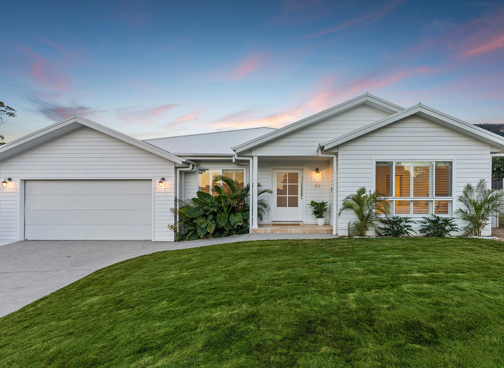 White House With a Garage, Green Lawn, and Tropical Plants Under a Twilight Sky — Evolution Building Group in Dapto, NSW