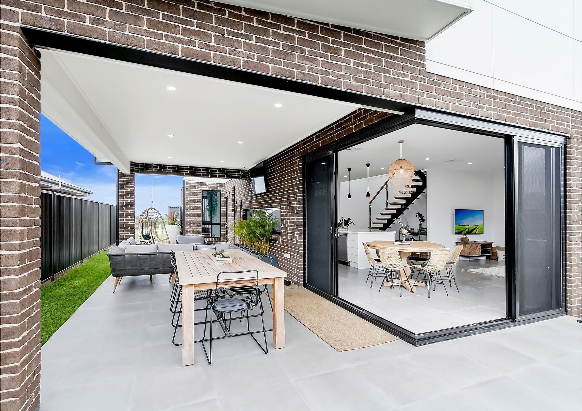 Patio with open sliding doors to a dining area; a wooden table with chairs, and brick and white building  — Evolution Building Group In Mittagong, NSW