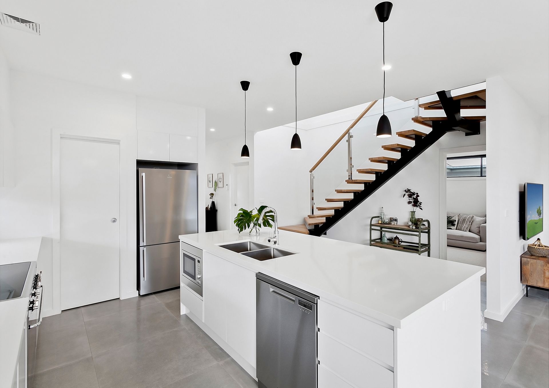 Modern white kitchen with a large island, stainless steel appliances, and a staircase leading to a second floor — Evolution Building Group In Shoalhaven, NSW