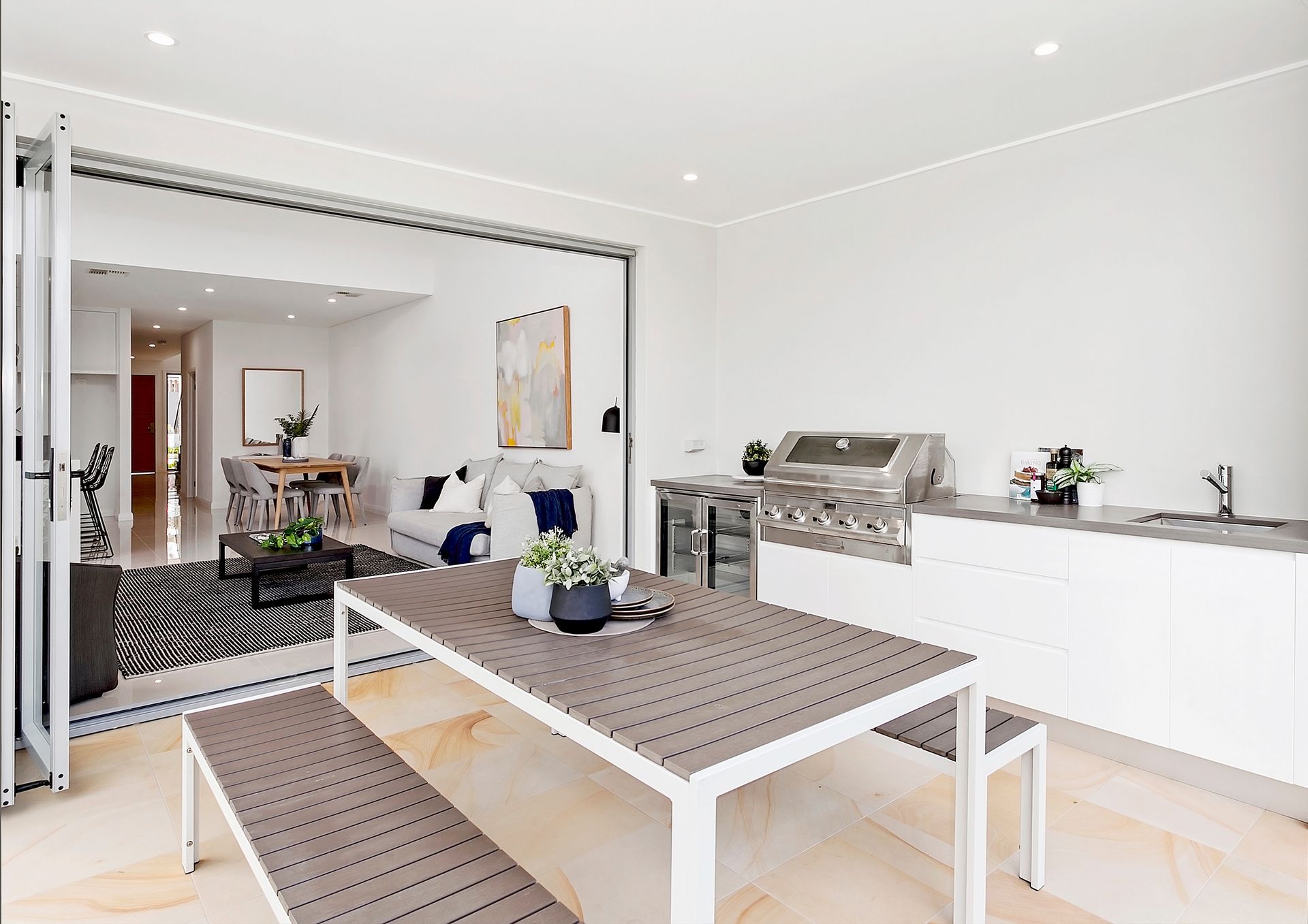An outdoor dining area connected to a living room. Features a table with benches, a barbecue, and an open doorway to a modern interior — Evolution Building Group In Moss Vale, NSW